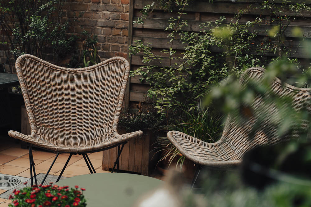 Hotel private garden courtyard with rattan armchairs and lush greenery in Bruges