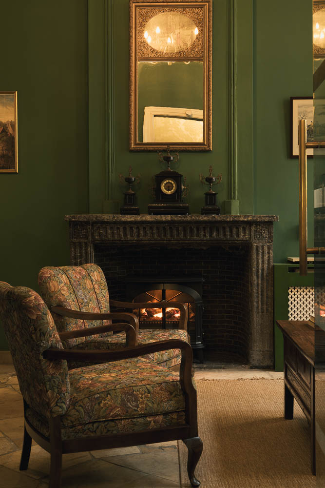 Hotel lounge with deep green panelled walls, antique armchair, and original marble fireplace