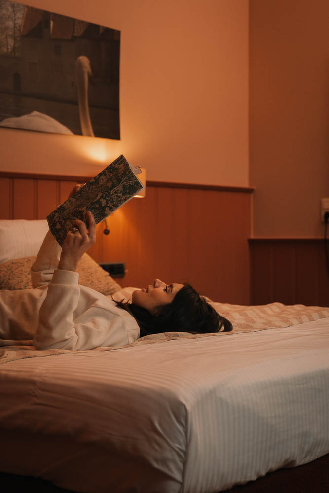Guest lying on a comfortable hotel bed reading a book in warm amber light